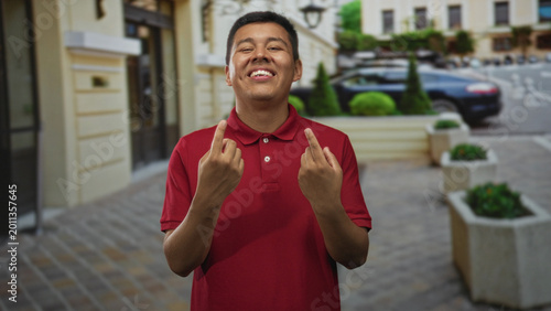 Foto Man in red polo shows both middle fingers smiling on cobblestone street outside building; defiance bold attitude