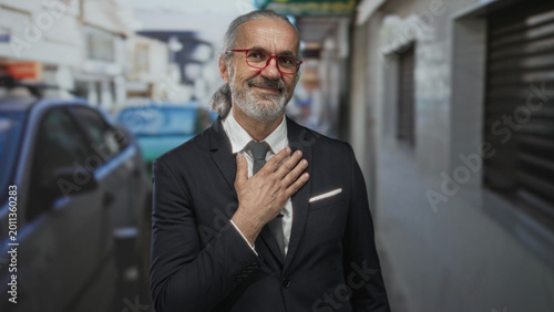 Photography Man in suit with hand on chest on street, gray hair and beard, red glasses and pocket square; gratitude respect