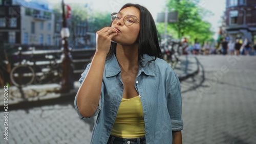 Картината върху платно Woman brunette in denim shirt flips hair with hand and purses lips on a cobbled street by a canal bridge; confidence attitude