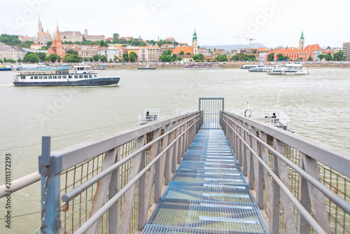 Fotografie View from a Budapest pier captures boats cruising on the Danube River toward the Buda side