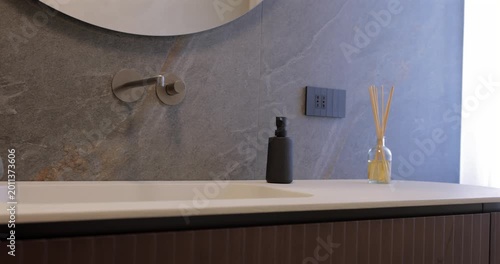 Contemporary bathroom vanity with ribbed natural wood and pale stone countertop, smooth camera glide follows curved cabinet beneath round mirror and built in wall faucet against dark stone