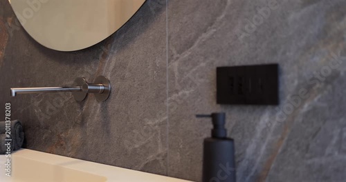 Modern bathroom interior with monolithic sink wood vanity and rounded mirror, slow camera pan reveals wall mounted faucet dark stone surfaces light countertop and soft daylight across a washroom