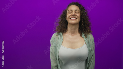 Tableau sur toile Young hispanic woman smiling with eyes closed wearing a white tank top in purple studio; contentment mindfulness presence