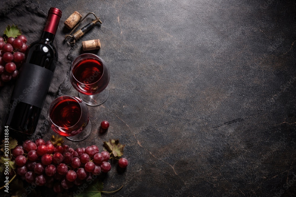Fototapeta premium Dark stone countertop featuring a wine bottle, grapes, and glasses with copy space from above