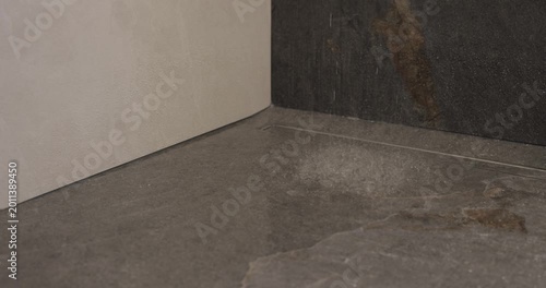Slow motion shower droplets striking dark stone floor in modern wet room, close video captures splashes and ripples around linear drain as water falls from above in premium minimalist bathroom setting
