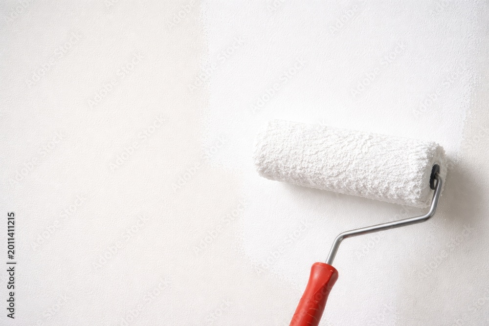 Obraz premium Paint roller with fresh white paint on neat wall featuring copy space for painting mockup