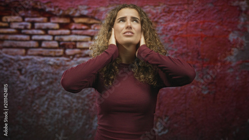 Canvas-taulu Young woman with curly hair pressing hands to ears and closing eyes against imagined noise in studio; anxiety