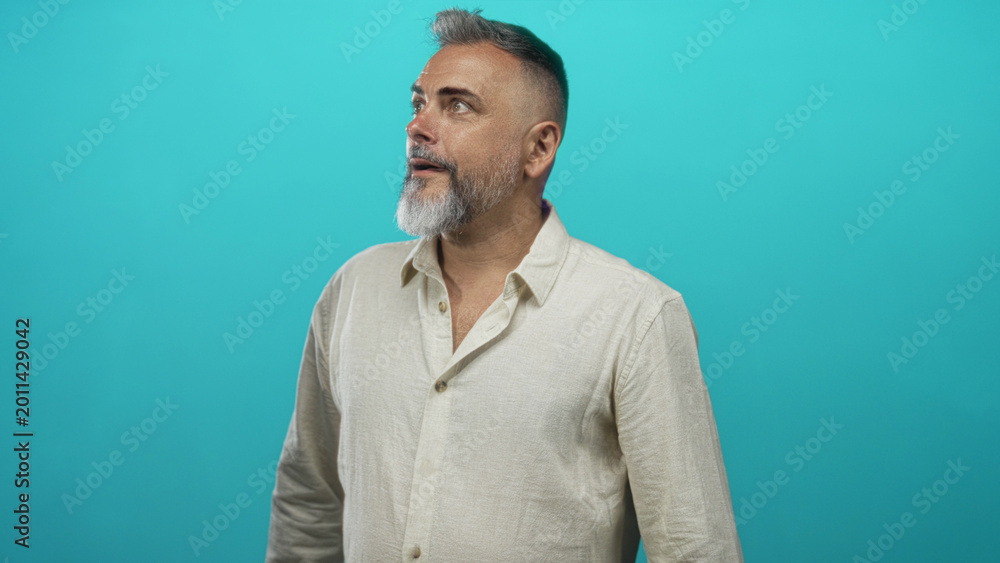 Fototapeta premium Man pointing right with finger in studio against turquoise backdrop, beige linen shirt visible and hand extended; curiosity.