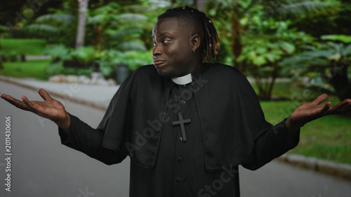 Photos Man priest shrugs arms with cross necklace on street, hands open in casual shrug; playful bemusement