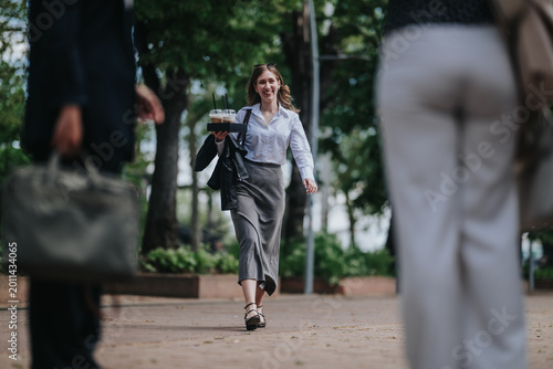 Photos A professional woman carries takeaway coffee while walking confidently between coworkers outdoors