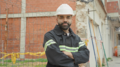 Photos Man architect in white hardhat and reflective vest with arms crossed at building construction site observing work; confidence oversight responsibility