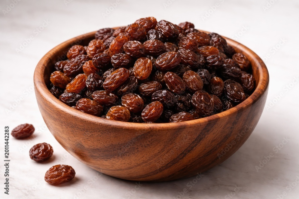 Fototapeta premium Natural wooden bowl holding a cluster of raisins on a smooth white backdrop