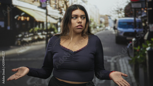 Foto Woman shrugs palms up showing cleavage and exposed midriff on a busy street with cafe seating and parked van, mouth open in surprise; confusion doubt