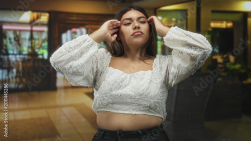 Foto Woman in white lace top with hand to forehead and closed eyes showing midriff in building lobby; fatigue release