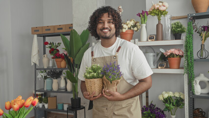 Man florist smiles while holding potted plants and woven basket with both hands in studio flower shop; serenity and care.