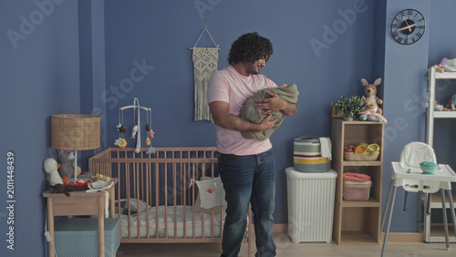 Foto Indian man cradling a swaddled baby with hands in studio nursery, smiling and gently adjusting the blanket; tenderness