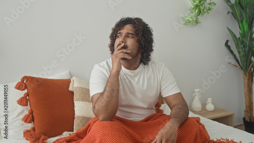 Obraz na płótnie Man on bed covering mouth yawning and rubbing eyes, orange blanket and white t shirt visible in a building; morning tiredness