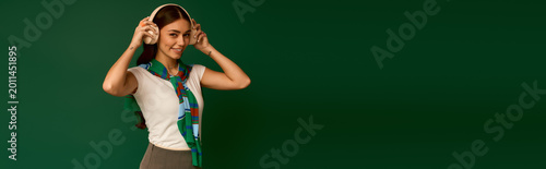 Vászonkép Stylish young woman in trendy outfit poses with headphones in vibrant green stud