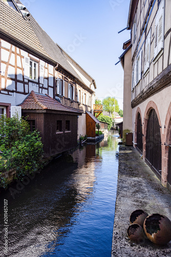 Traditional half-timbered houses along a narrow canal in Wissembourg, France, creating a peaceful and picturesque old town atmosphere.