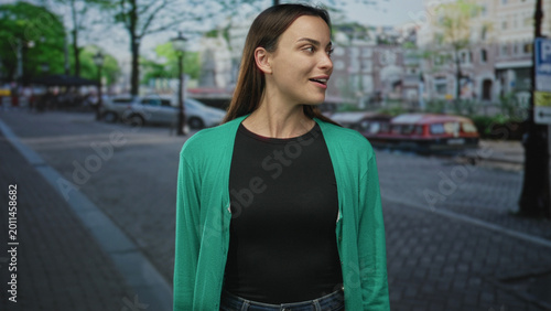 Schilderij op canvas Woman with mouth open looking sideways on street by canal boats, wearing green cardigan and black top, profile view; surprise curiosity