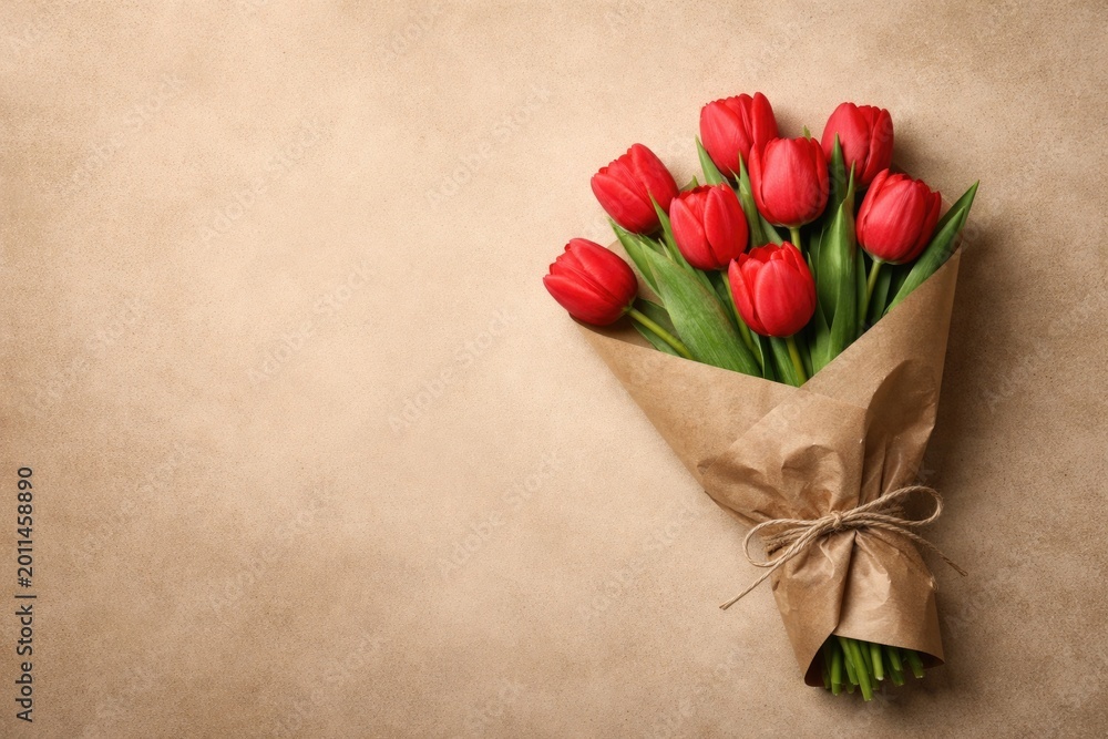 Fototapeta premium Beige backdrop featuring a red tulip bouquet wrapped in recycled craft paper with copy space from above