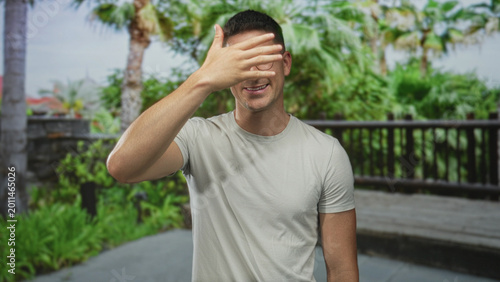 Foto Man, young hispanic, wearing glasses and a white t shirt, placing hand on chest on a street outdoors near wooden railing; sincerity trust