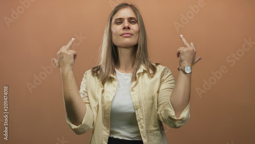 Εκτύπωση καμβά Blonde young woman shows both middle finger gestures wearing white tank top and beige shirt in orange studio; defiance attitude