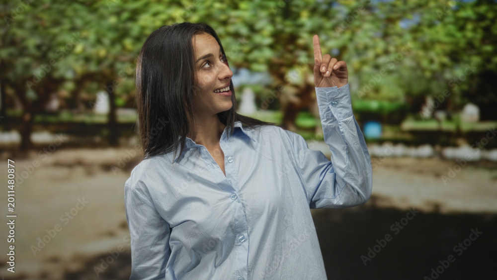 Fototapeta premium Woman showing ok sign with fingers and smiling in forest setting wearing light blue shirt; joy approval.