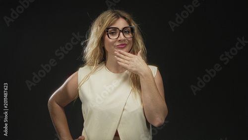 Foto Woman with hand on chin and glasses in black studio, wearing sleeveless cream top, pensive expression; quiet confidence
