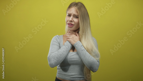 Bild auf Leinwand Woman clutching throat with both hands, grimacing, young blonde in gray top in studio; distress emergency breathlessness