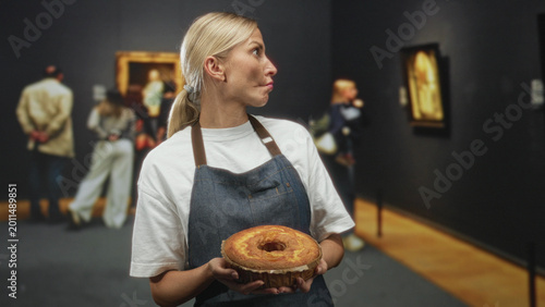 Foto Woman holding sponge cake with both hands in a museum building, head turned and lips pursed in a playful pout; playful contrast