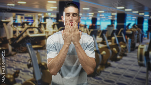 Foto Man blows kiss hand to mouth in gym among treadmills and weight machines wearing striped t shirt; affection playful moment
