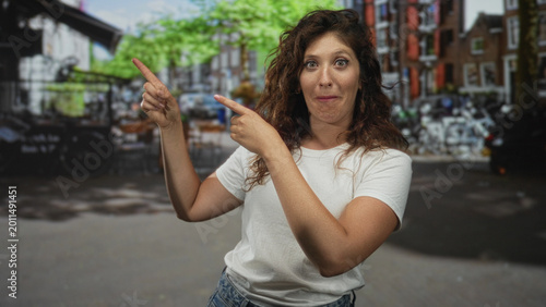 Photos Woman points both index fingers on street, hands and freckled forearms visible while smiling; playful curiosity