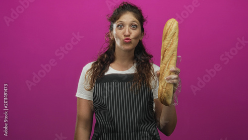 Canvas Print Woman puckering lips holding baguette with gloved hand wearing striped apron in studio vibrant pink backdrop; playful baking