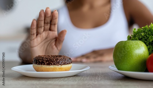  Close up female using hand push out her favourite donut and choose green apple and vegetables for good health 