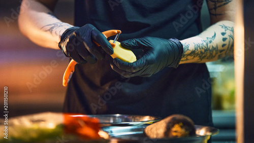 Foto Chef peeling potato with orange peeler in moody restaurant kitchen