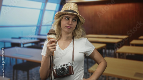 Bild auf Leinwand Woman holds ice cream cone and vintage camera in a classroom building with hand on hip; boredom travel