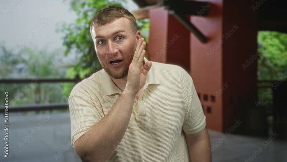 Fototapeta premium Man cups hand to ear in building, leaning forward with visible hand and face, listening gesture; surprise curiosity.