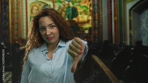 Canvastavla Woman giving thumbs down gesture toward camera in ornate church building nave with pews and painted iconography; disapproval protest