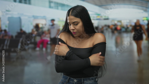 Canvastavla Young latina woman in black off shoulder top hugs arms across chest at busy airport terminal; unease