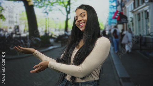 Schilderij op canvas Young latin woman smiles while holding out both hands with palms up on urban street in daylight; invitation