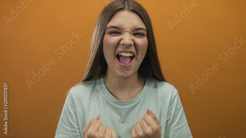 Foto Teenage girl in mint green tshirt clenches fists confidently in studio with orange backdrop; enthusiasm