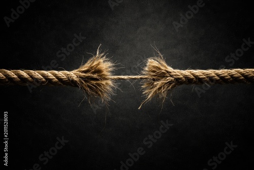 Strained rope fiber conveying precarious hold and uncertainty on black textured base with copy space