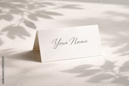 Wedding place card mockup with a folded white name card casting leaf shadows on a plain background