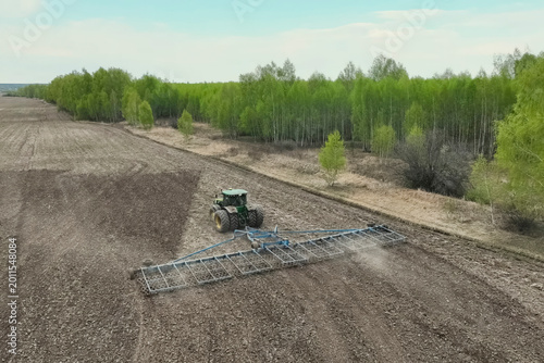 Картината върху платно tractor with plow harrows and plows the soil in the field