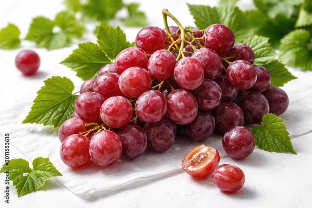 Obraz premium Red globe grapes paired with green leafy sprigs arranged on a crisp white setting featuring vivid color and detailed texture