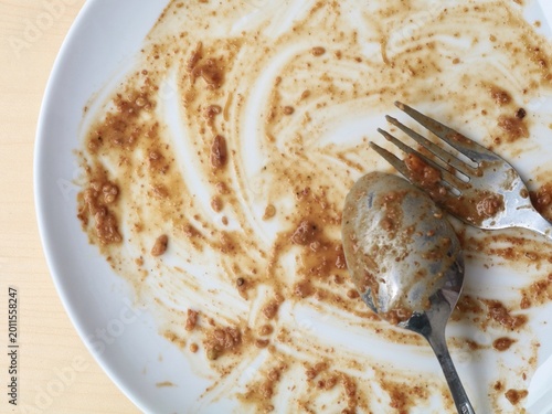 Dirty empty plate with spoon and fork after meal finished, represents the end of a delicious meal, food waste, or the need for dishwashing