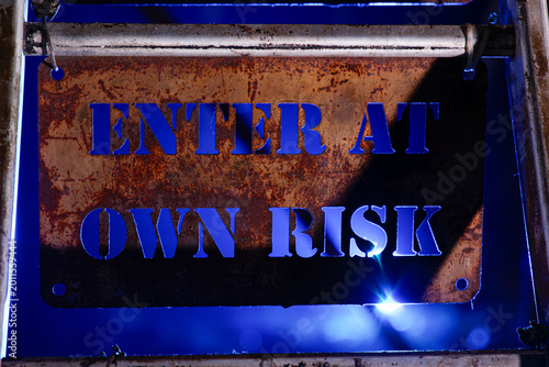 Schilderij op canvas Rusty metal warning sign reading enter at own risk with blue lighting and industrial background, conveying danger and restricted access