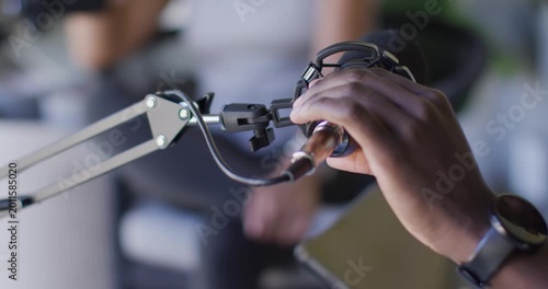 African American hosts man adjusting studio mic on boom arm, plugging XLR cable, prepping recording