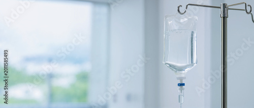 IV drip bag hanging on a metal pole in a hospital room. Intravenous saline solution for patient treatment. Medical infusion therapy concept